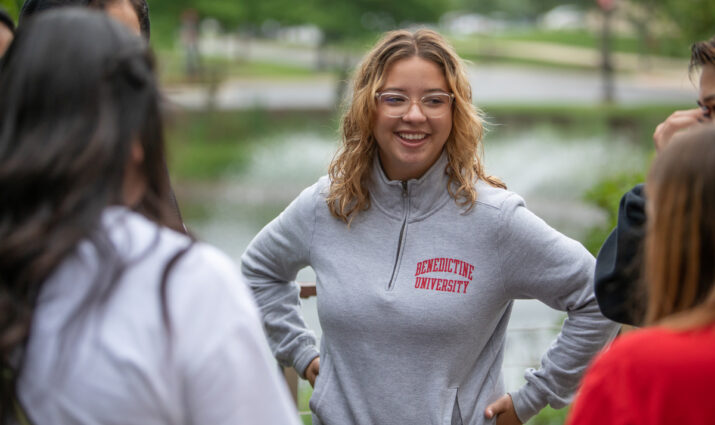Female alumni with Benedictine University sweatshirt speaking to a group of visitors - Alumni volunteer