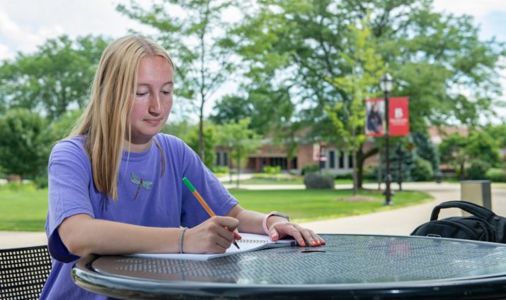 Female student taking notes at a table outside in the quad