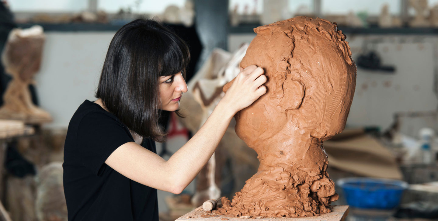 female art student working on a clay sculpture of a head; fine arts