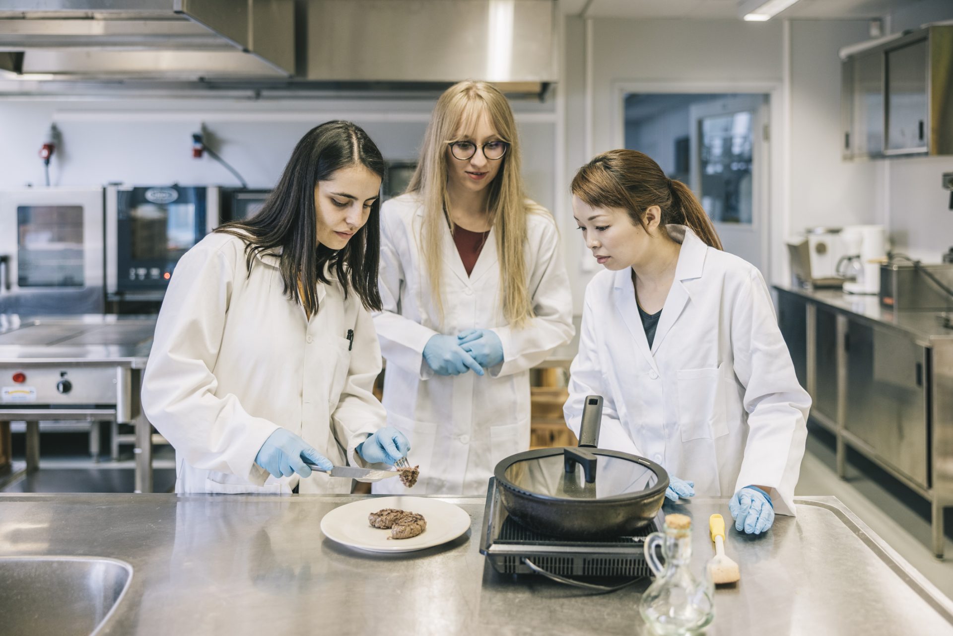 three Female scientists looking at genetic meat in laboratory kitchen.