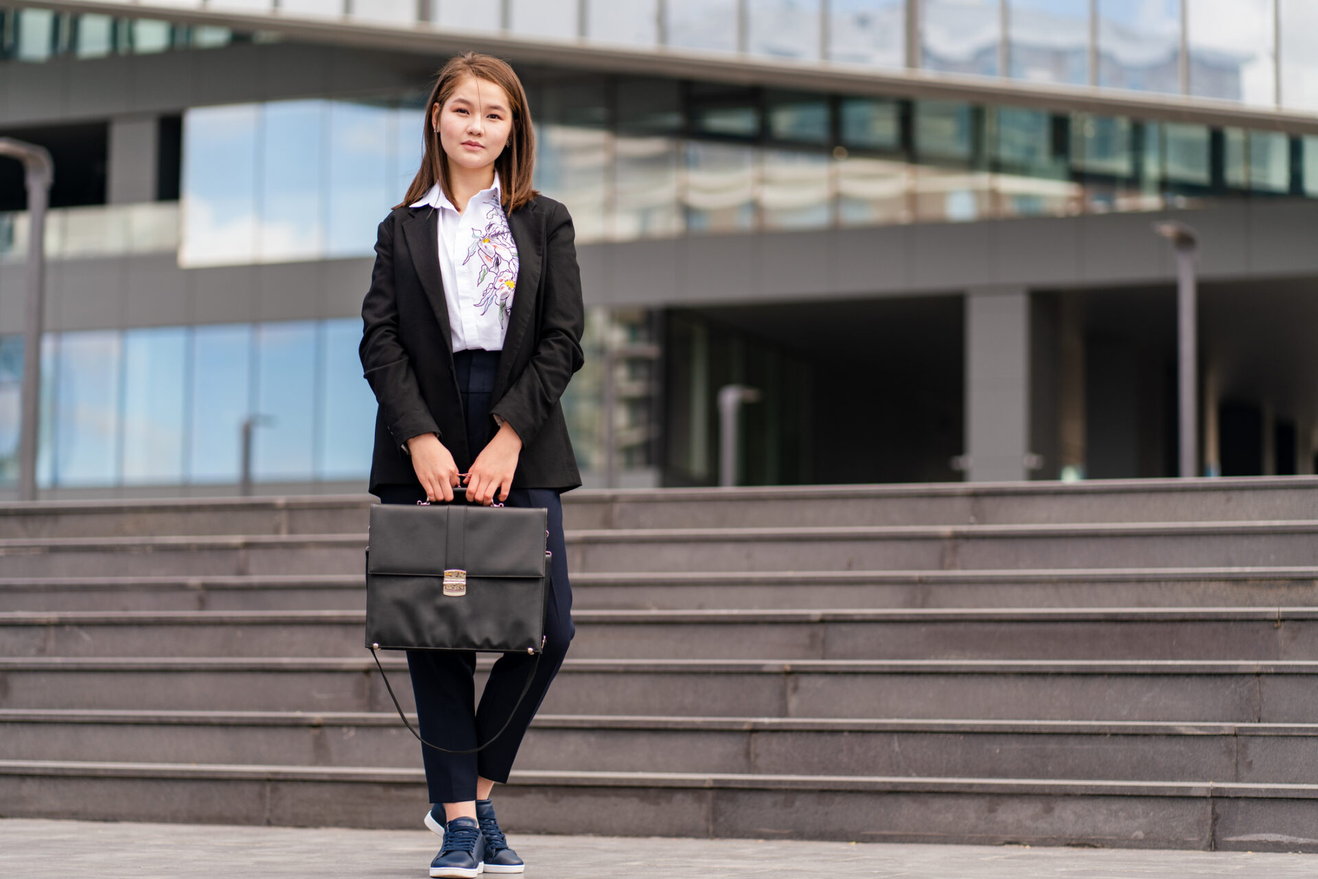 Asian businesswoman portrait standing with briefcase at foot of stairs of building; political science