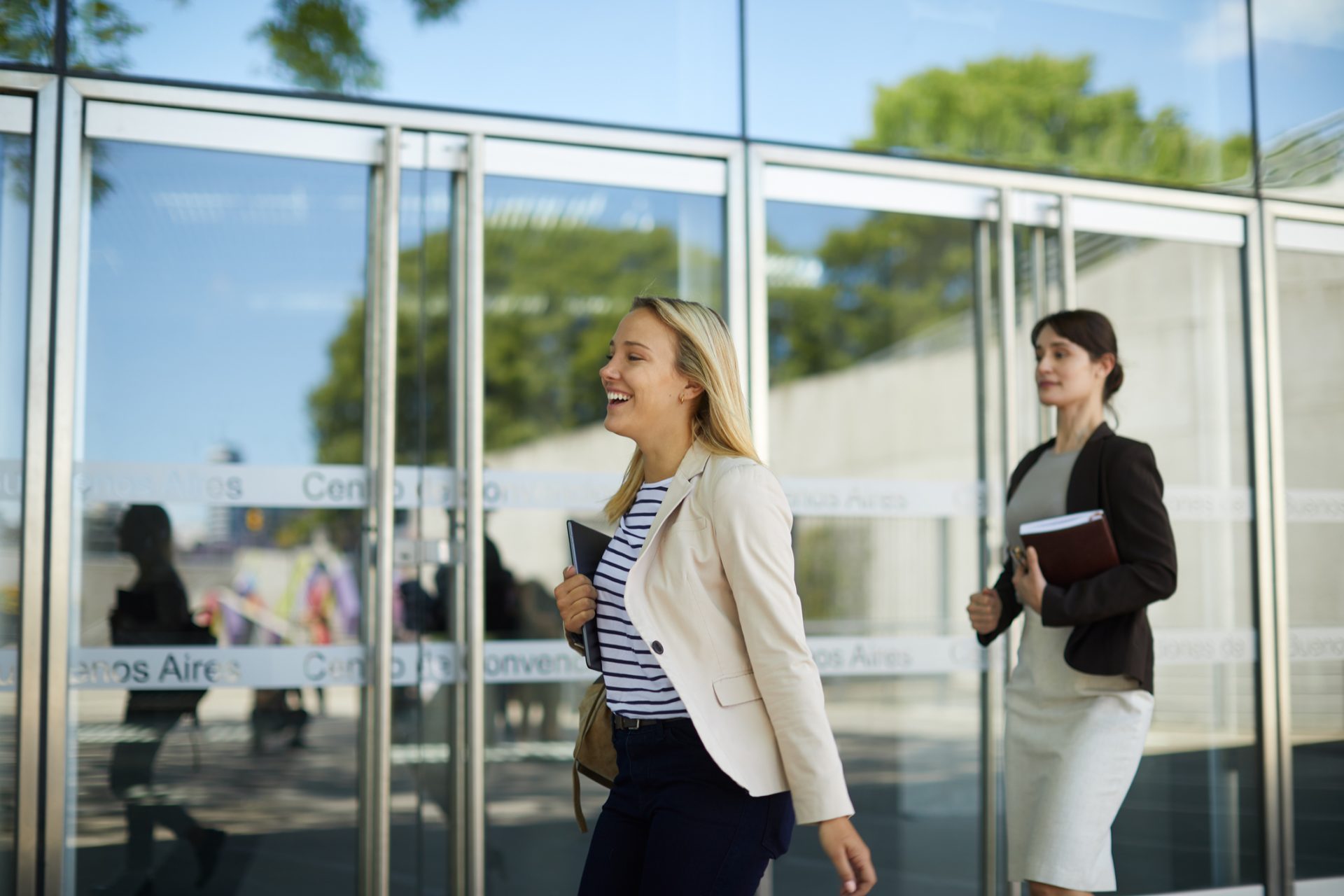 female student holding notebook and smiling waling past glass doors; Political Science