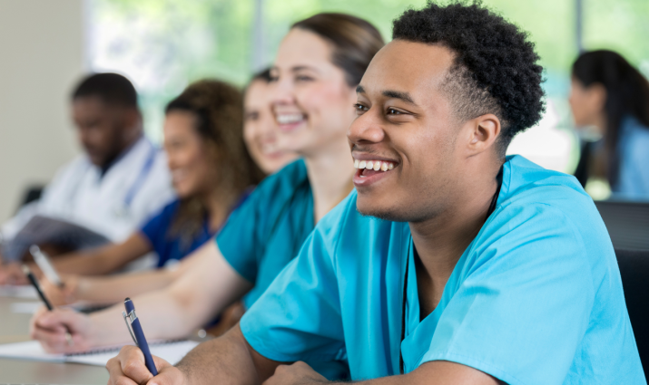 multi-racial group of medical student sitting in a row; male student in foreground clear and smiling; pre-medicine