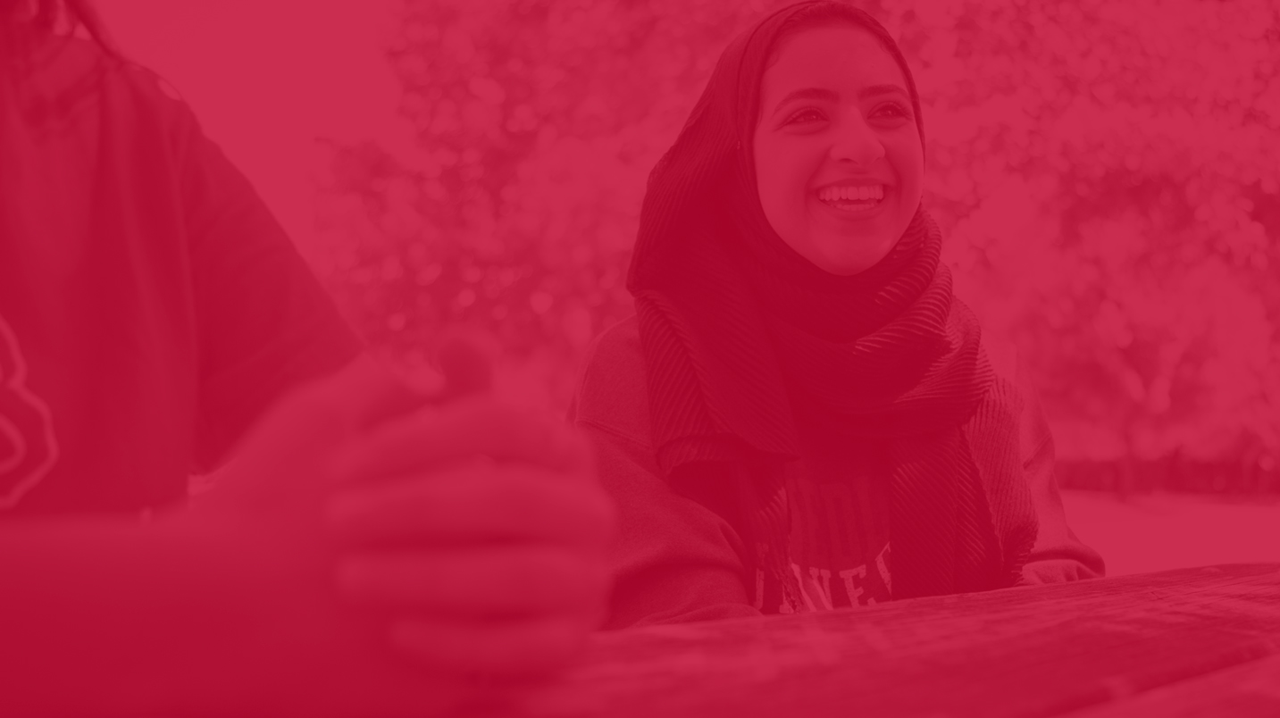 female student with headscarf smiling, photo has red overlay on it