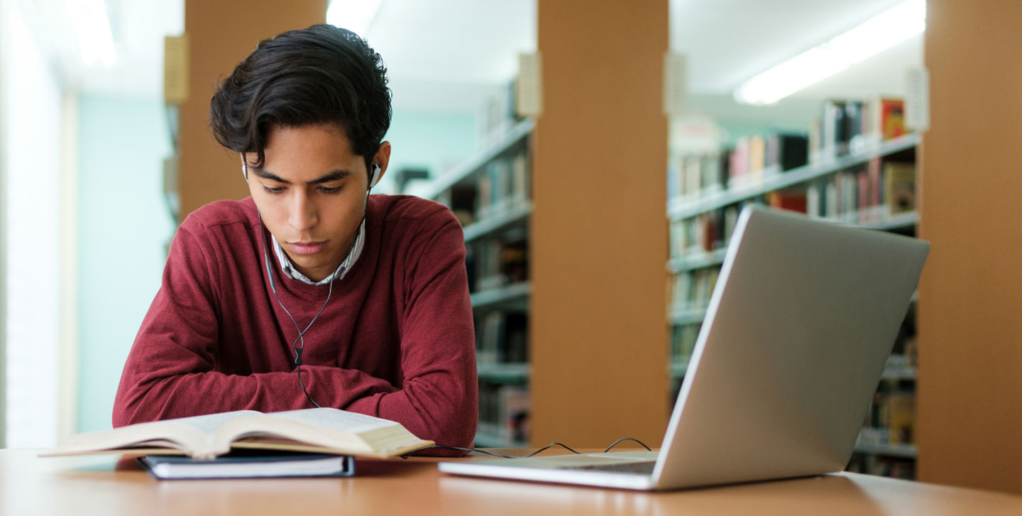 male student with ear buds studying in the library; English Language and Literature