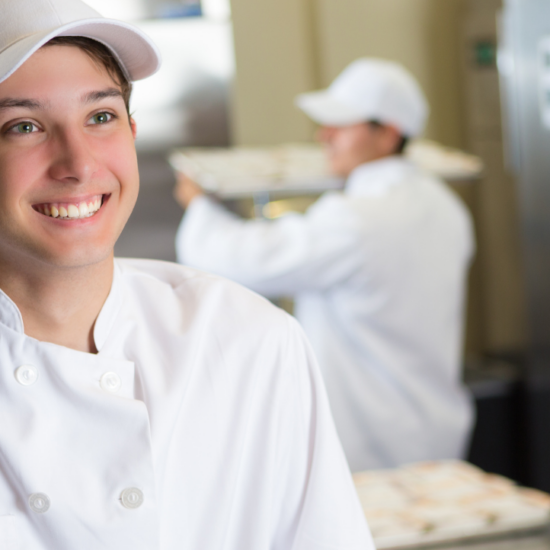 young chef with chef coat and hat smiling in kitchen; nutrition and food management