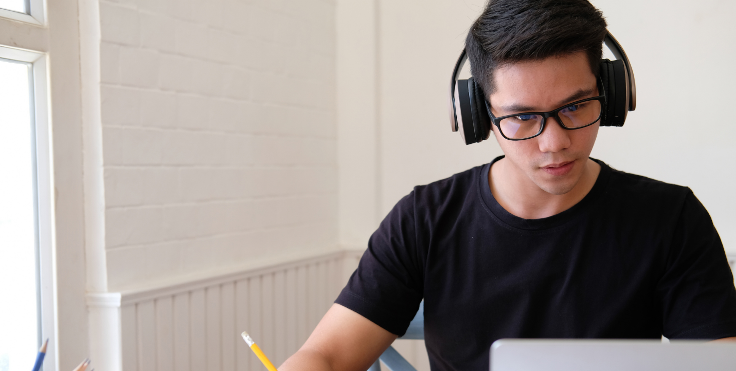 male student with headphones studying on his computer; Spanish