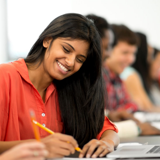 female student smiling while taking notes at her laptop; writing and publishing program