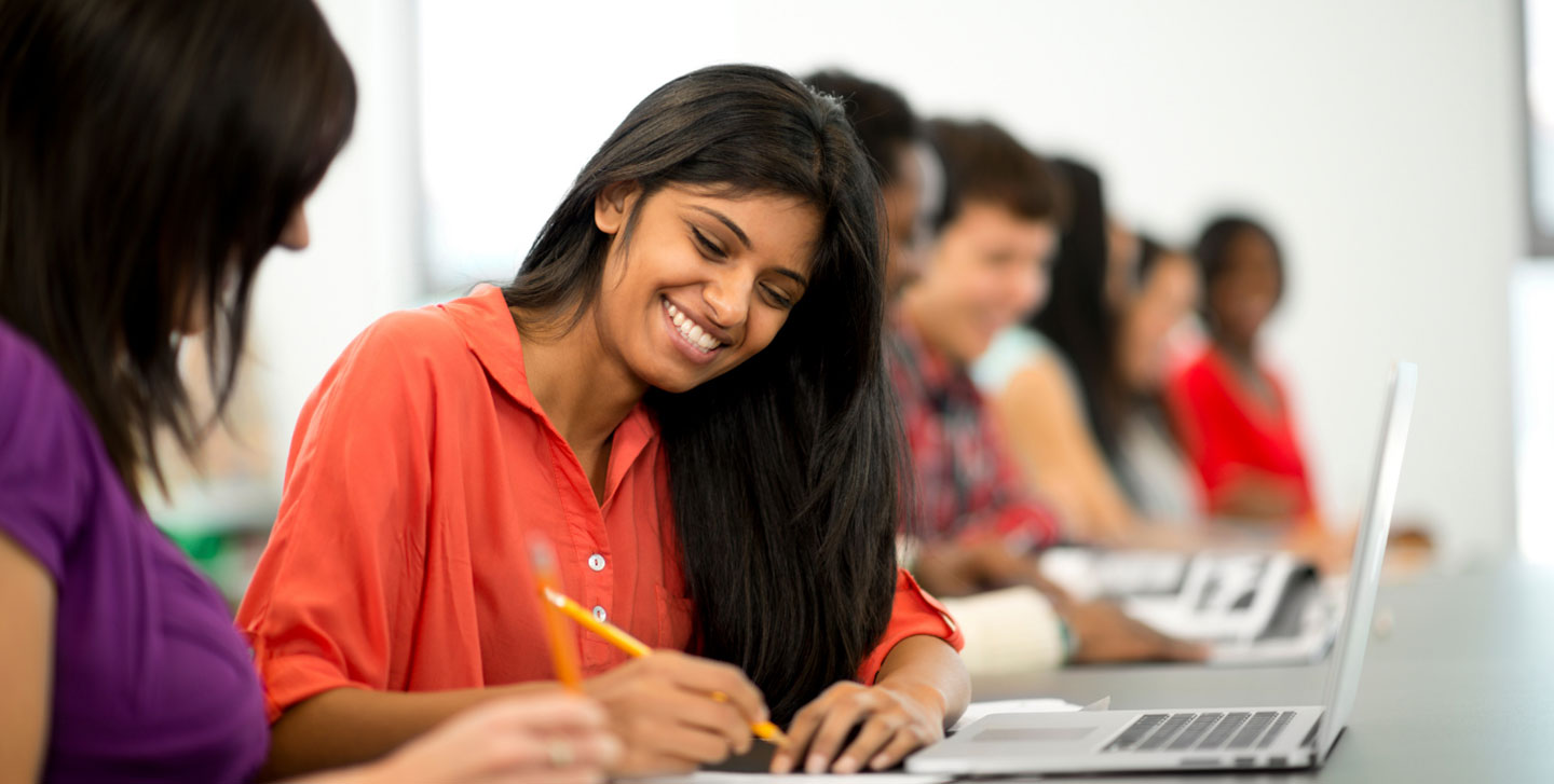 female student smiling while taking notes at her laptop; writing and publishing program