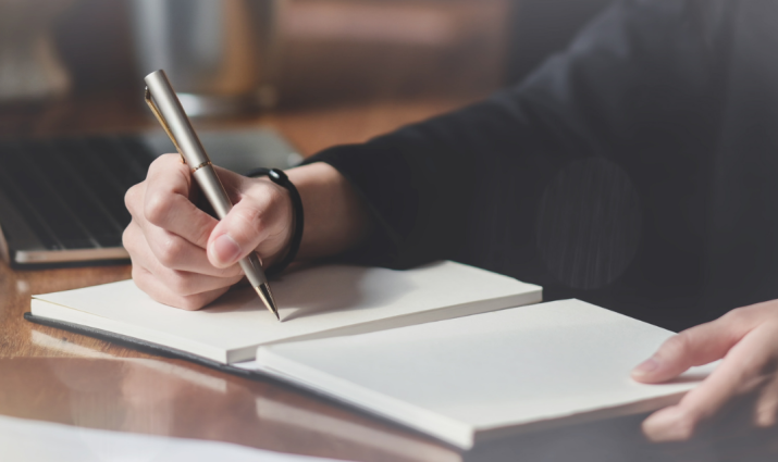 handing holding pen writing in notebook; writing and publishing program