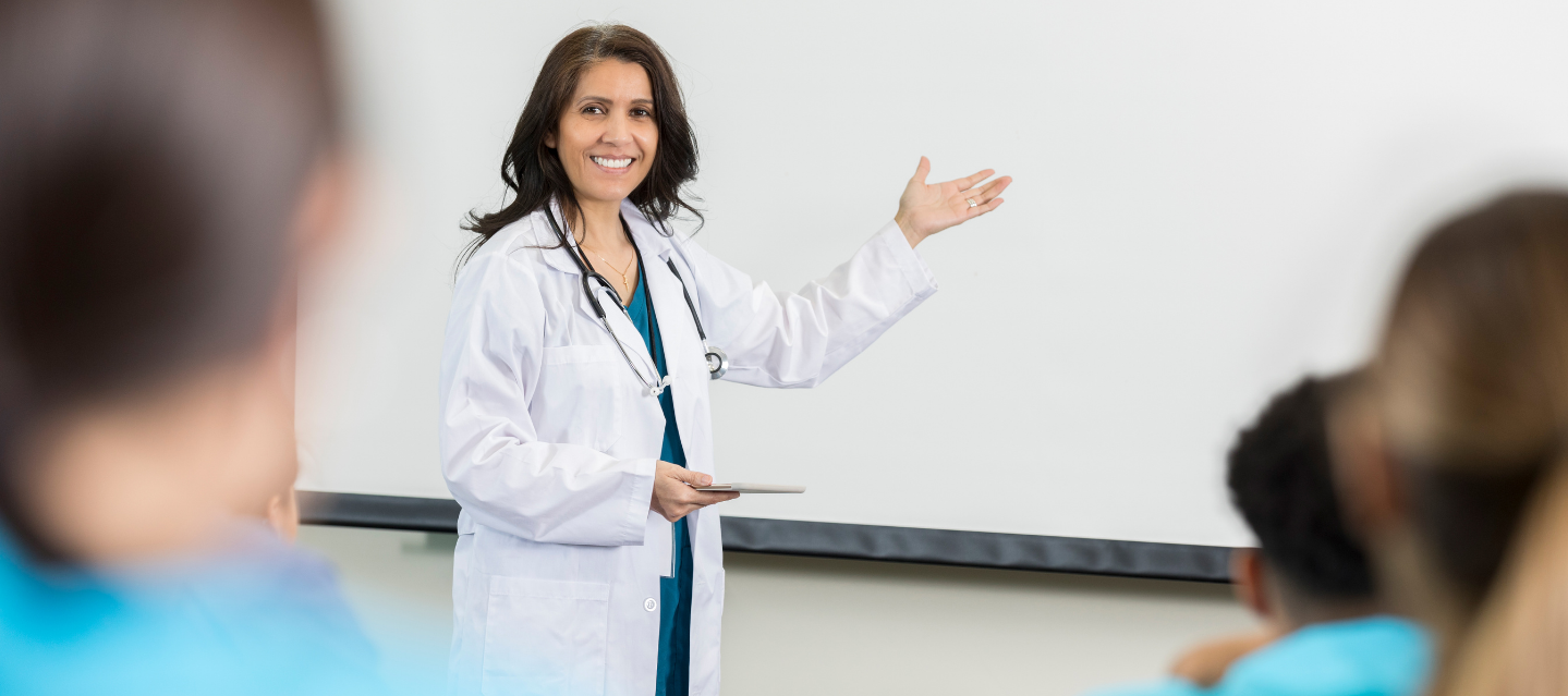 female instructor in lab coat with stethoscope lecturing in front of class