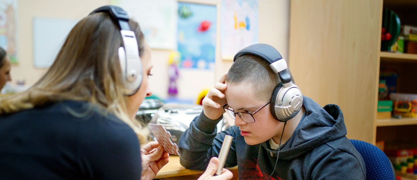 special education teacher working with special needs student, both wearing headphones; special education