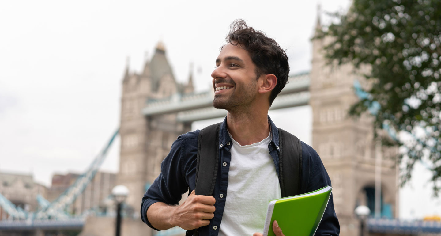male student with notebook standing in front of the London bridge; linguistics