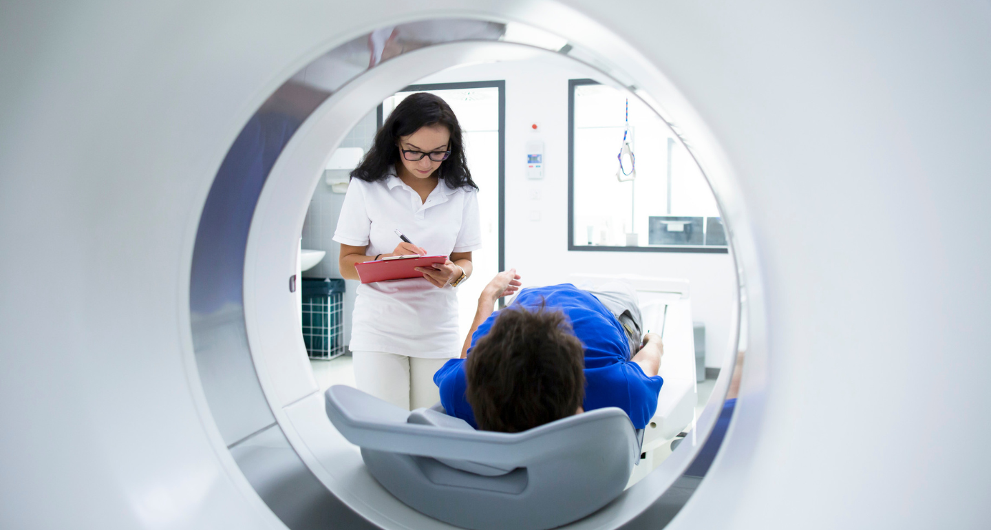 female tech writing on a clipboard as patient waits to enter an MRI machine; nuclear medicine technology