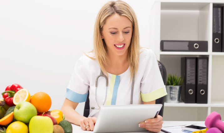 female dietician holding paperwork with bowl of fruit on the table with her; nutrition and wellness MS program