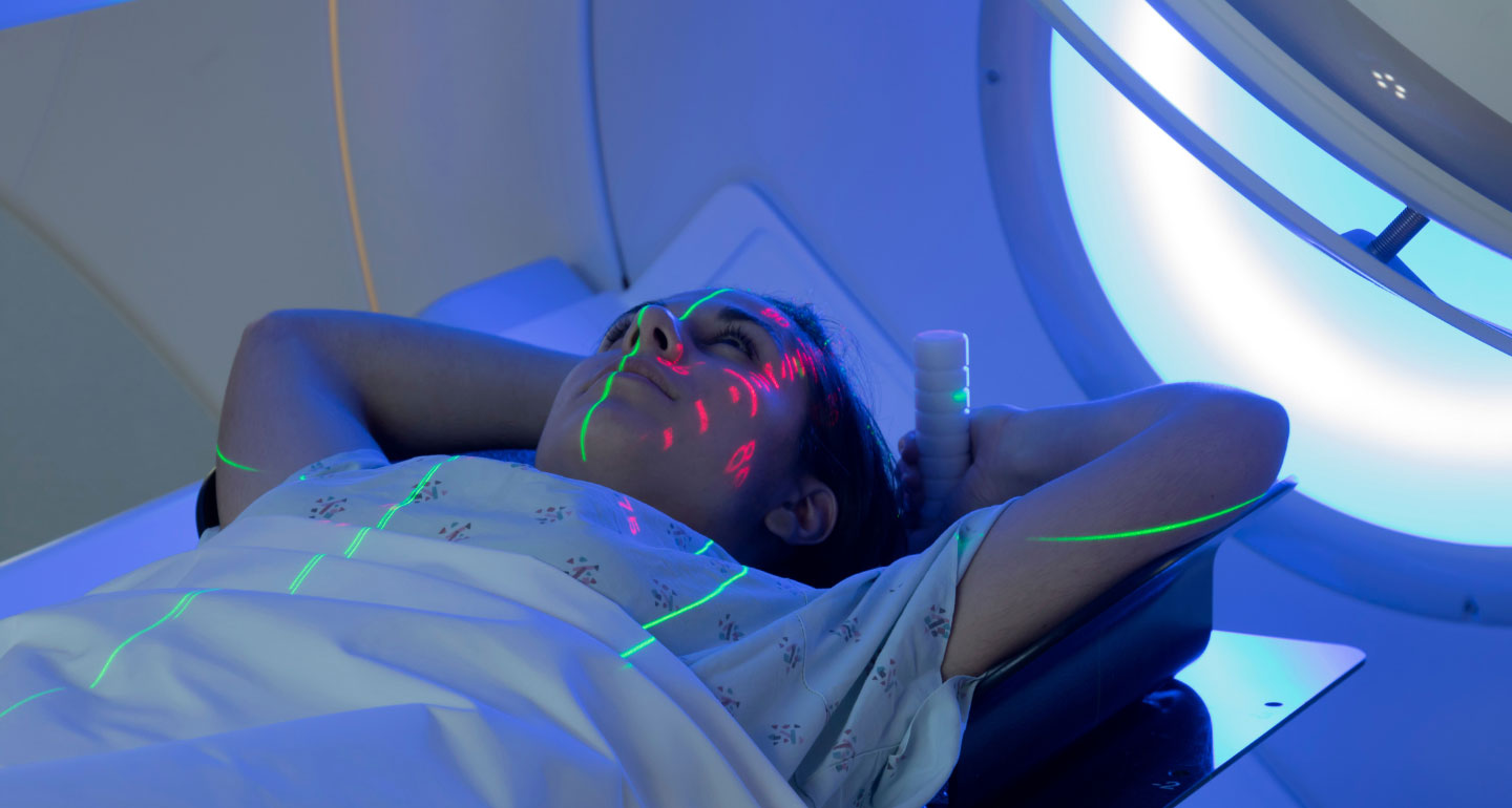 image of person in an MRI machine, hands above their head with lights mapping their upper body; radiation therapy