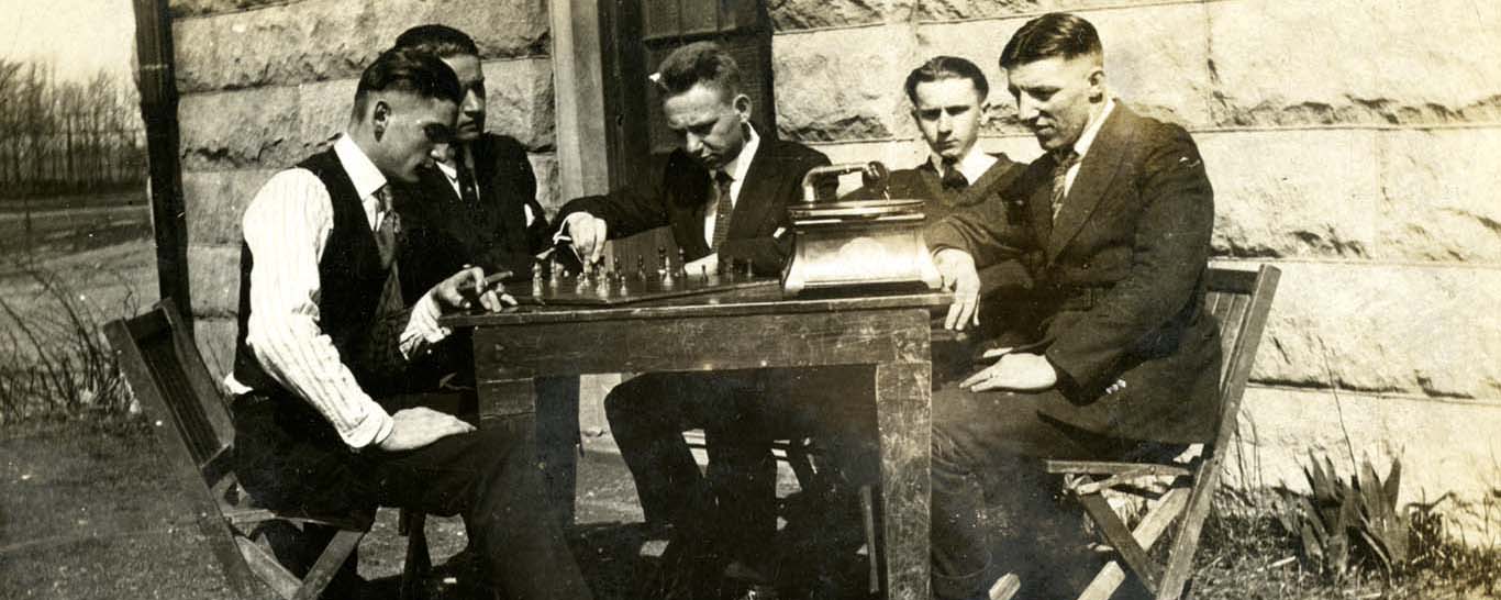 Historic black and white photo of five men sitting at a table outside of Ben Hall