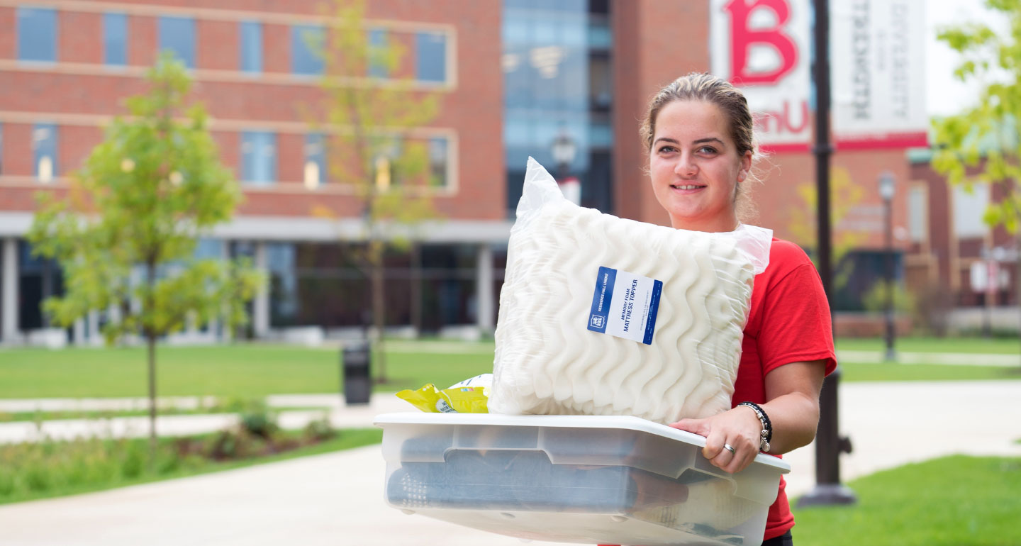 female student holing crate and pillow moving into dorm room
