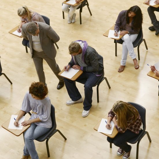 overhead view of students at desks taking an exam with a professor looking over the shoulder of one student