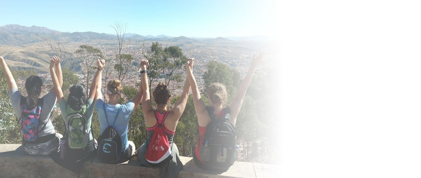 Students sitting on a ledge overlooking beautiful scenery, holding hands above their heads