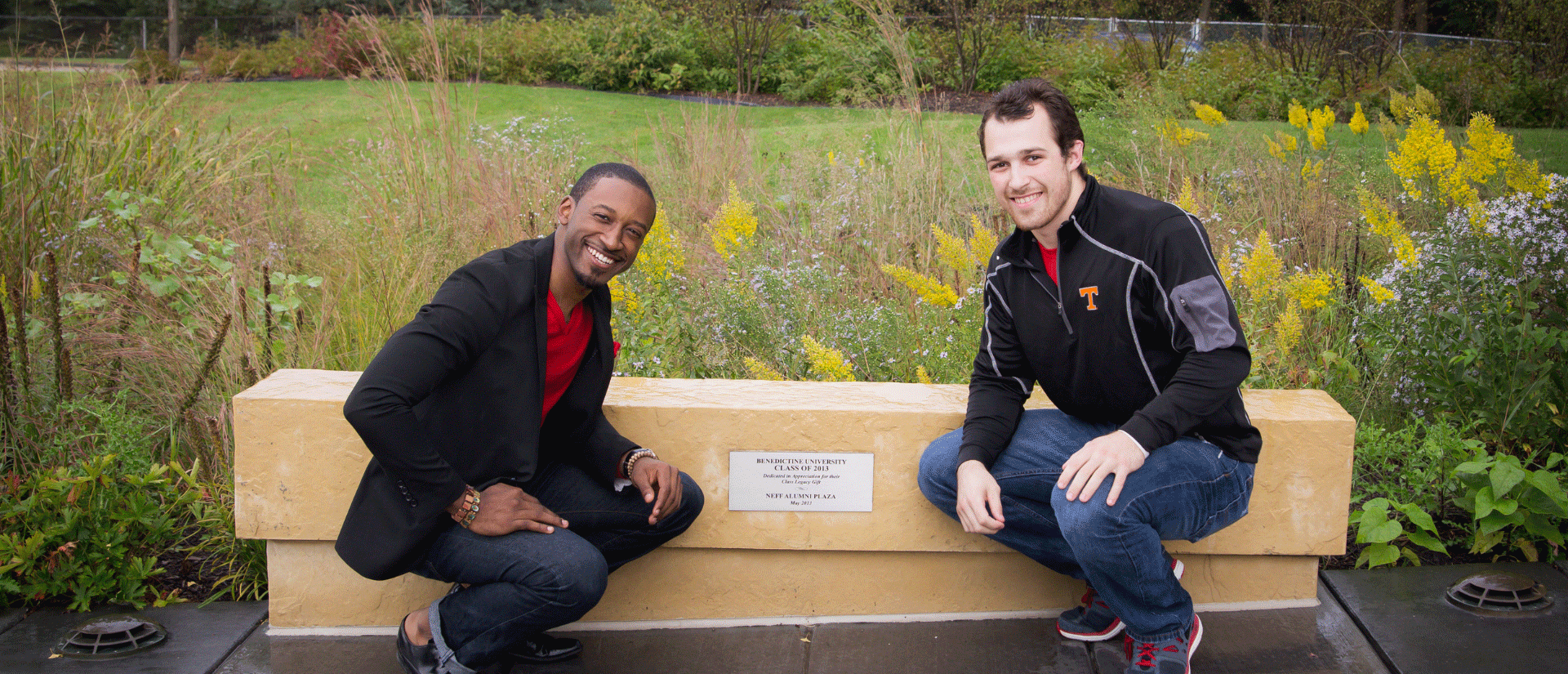 alumni students sitting by bench dedicated to their class