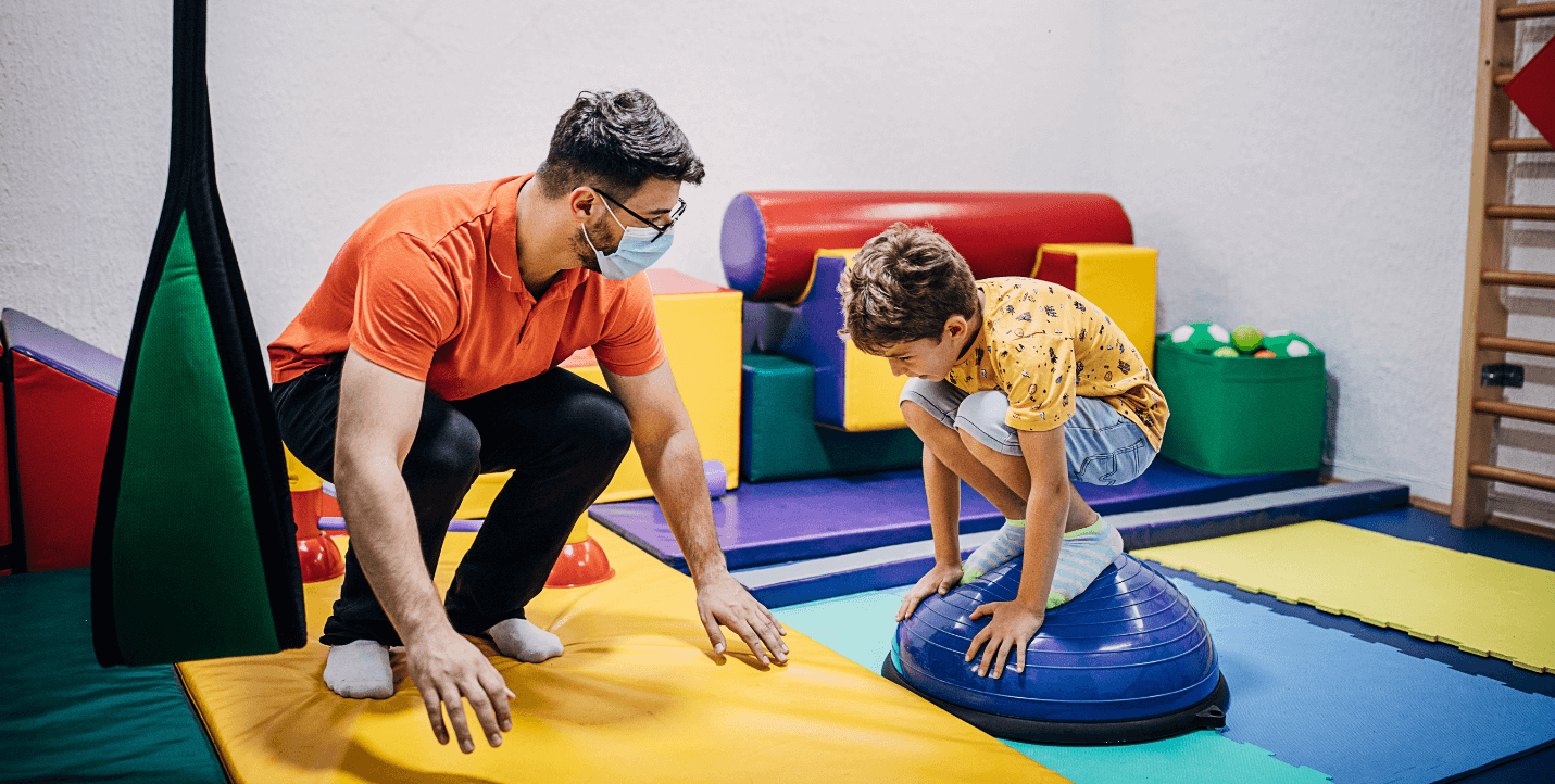 male student working with younger child on physical therapy ball