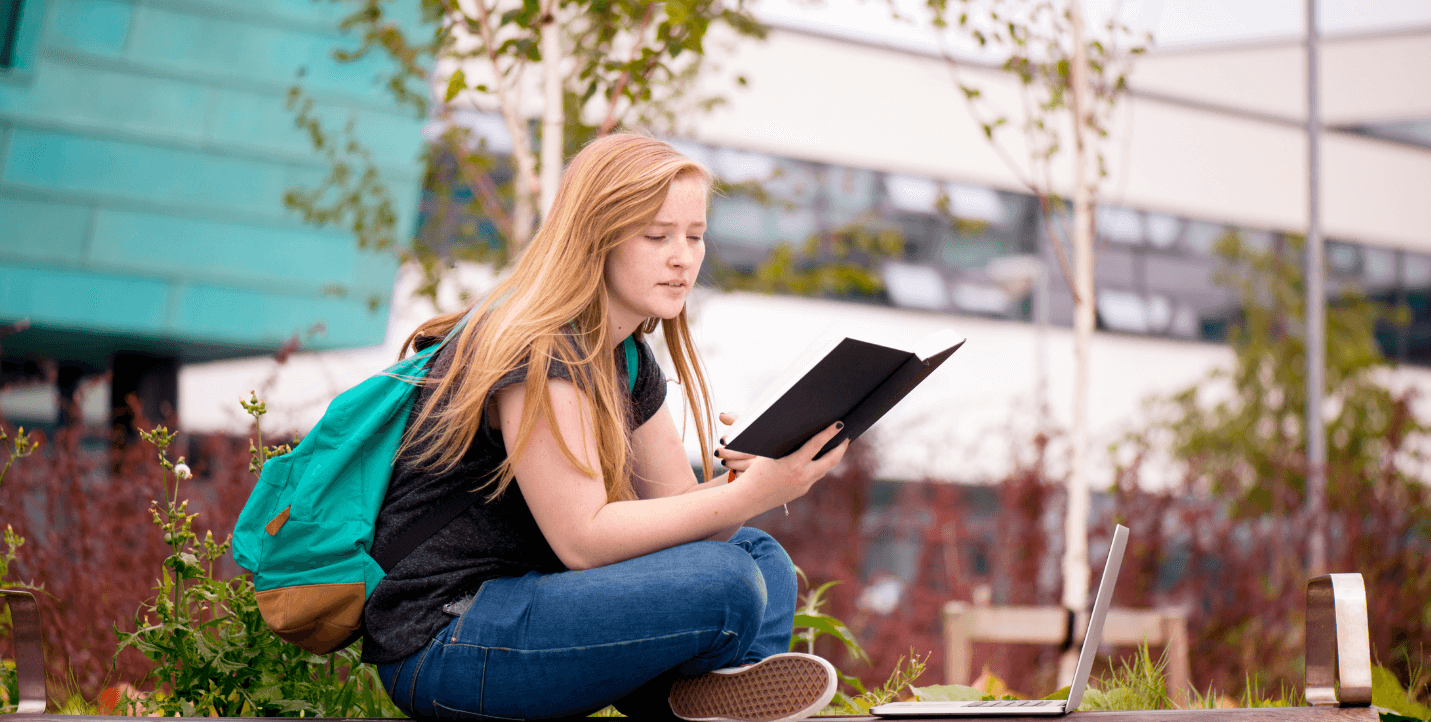 female student reading book while sitting on campus