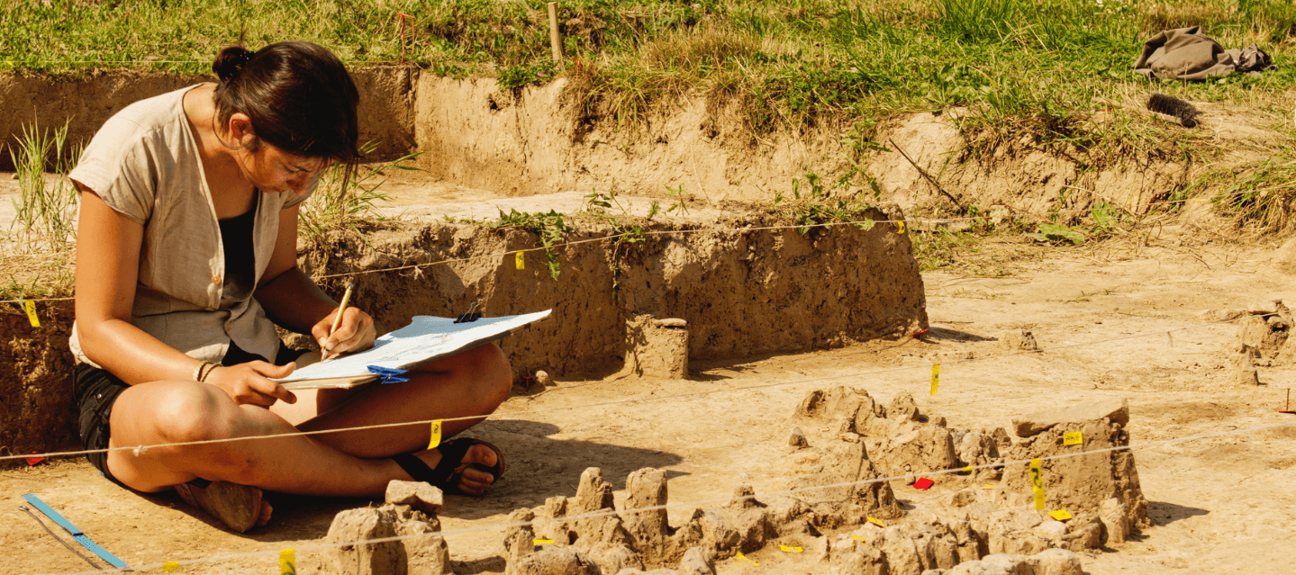 girls sitting outside in an archeological dig site with clipboard