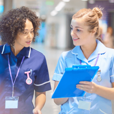 female nurses, one sharing clipboard with the other