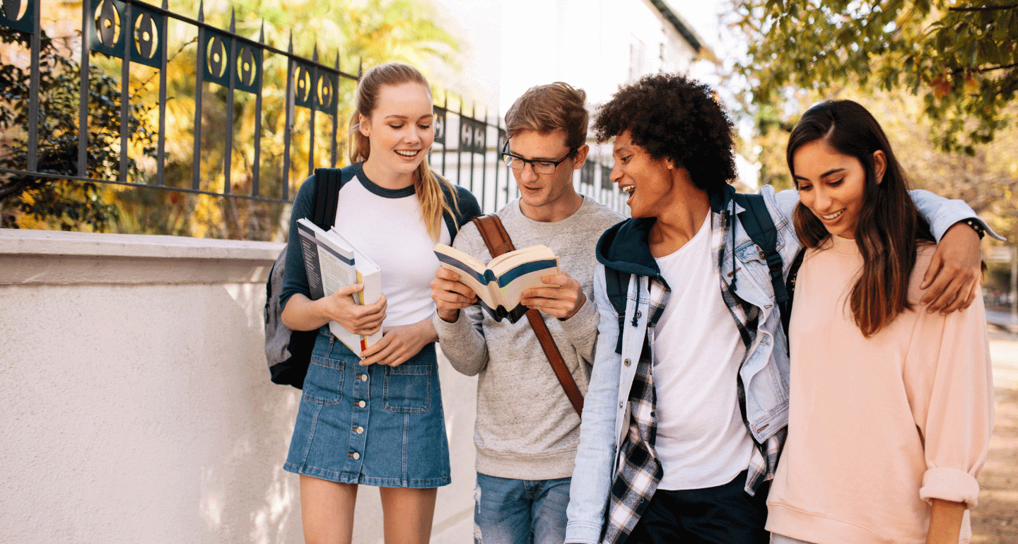 four students walking on campus one reading book to the others