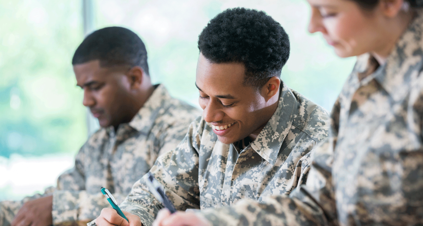 Military scholarships. military personnel writing at table. Middle male is smiling while writing.