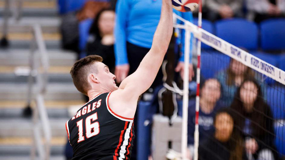 Men's volleyball player spiking ball at net