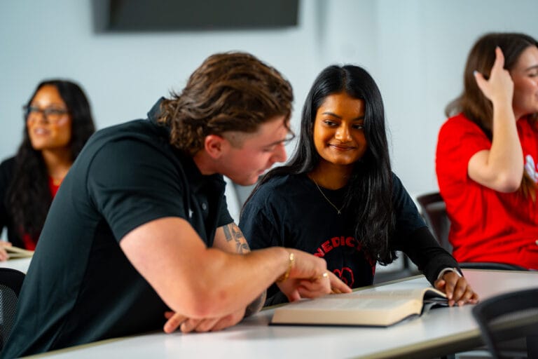 Two students reading from a book in class.