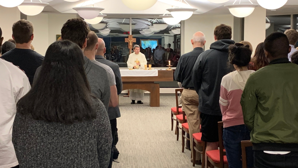 A group of people standing in a room with a priest.