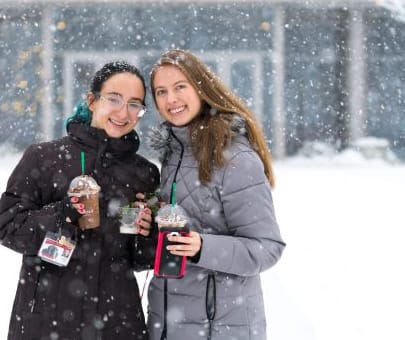 two female students holding coffee in the snow on Lisle campus