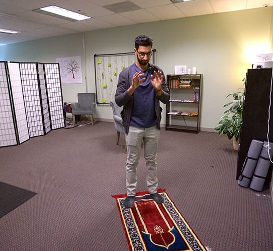 A man standing on a rug in the interfaith prayer room