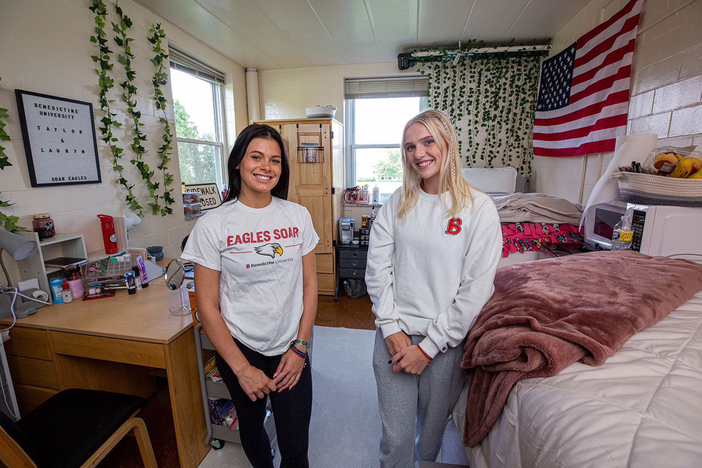 Two women standing in front of a bed in a dorm room.